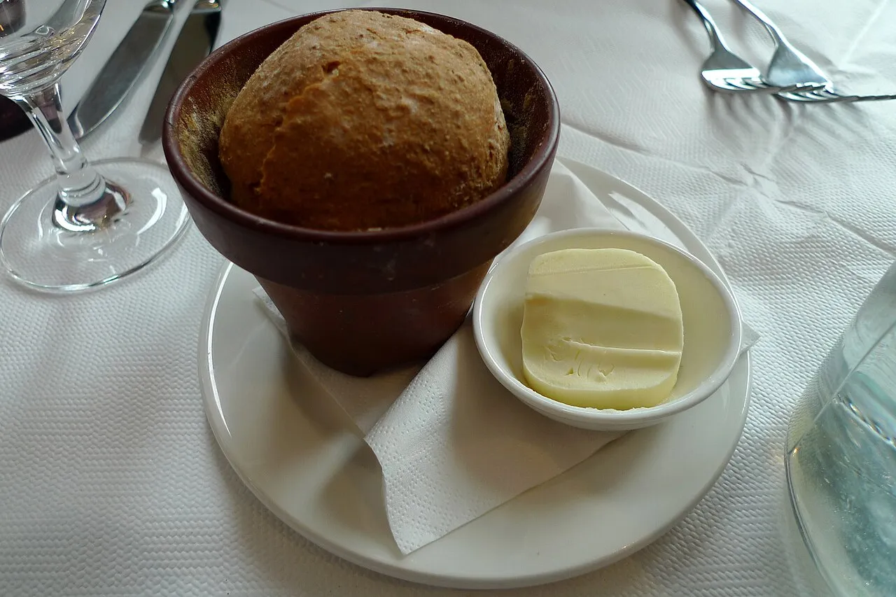 Placeholder stock photo: A round loaf of bread served in a small terracotta flower pot with butter
